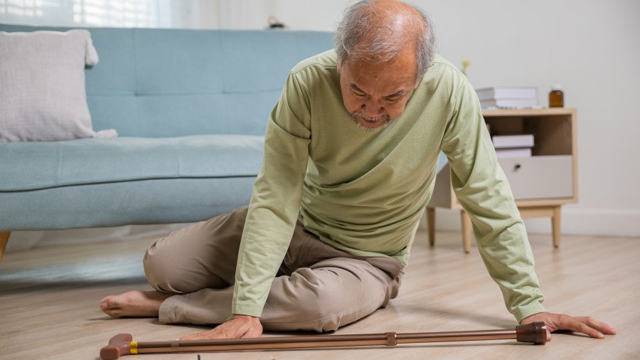 Senior man lying on floor in living room with wooden cane walking stick because he fell