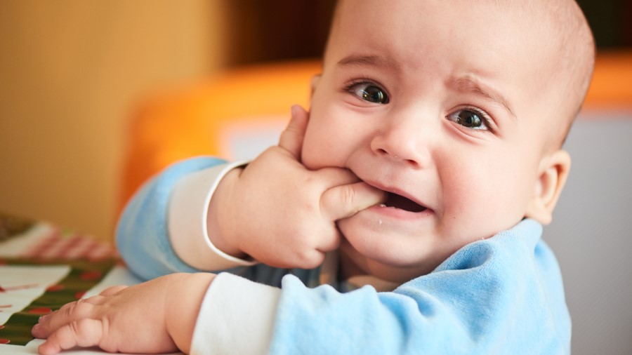 Close up of a baby boy who is crying and has his fingers in his mouth because he is teething